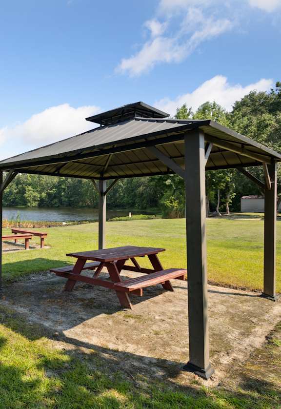 Picnic table and pavillion in a park with a lake in the background.