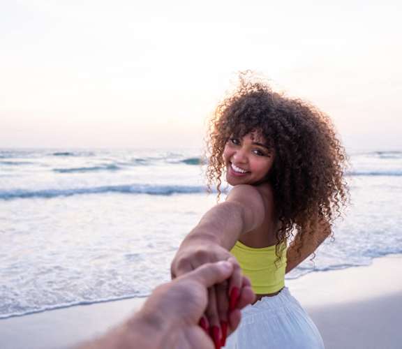 a woman holding the hand of a man on the beach