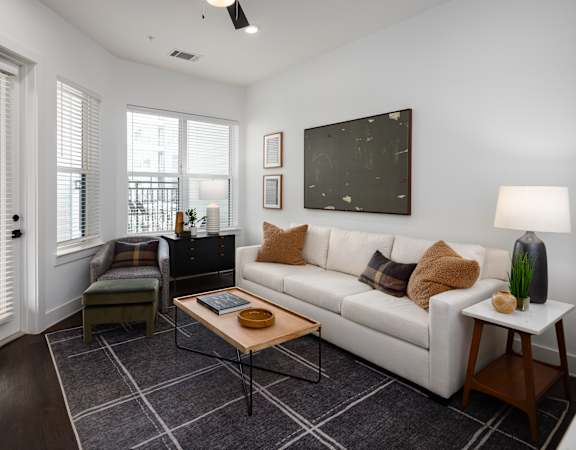 A living room with a white couch, a wooden coffee table, and a large window with blinds.