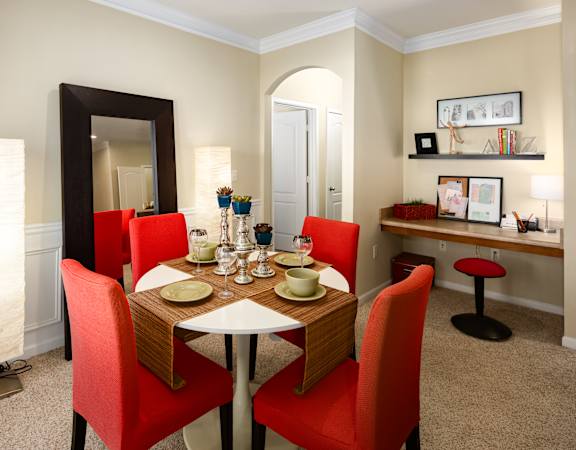 A dining room with a table set for two and red chairs.