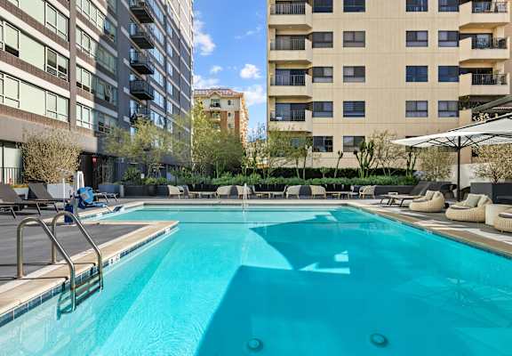 a swimming pool with lounge chairs and umbrellas in front of an apartment building at The View, Los Angeles