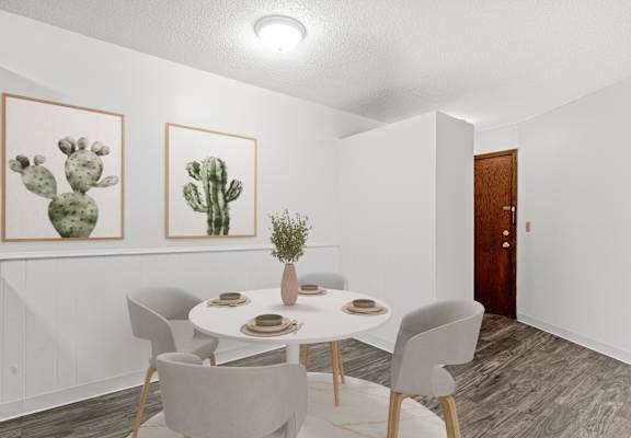 A dining room with a table set for two and two cactus pictures on the wall.