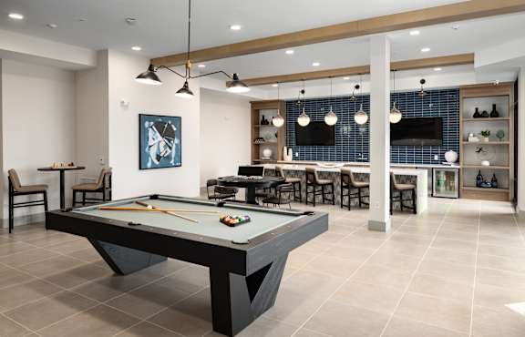 A pool table is in the middle of a room with a bar and a TV.