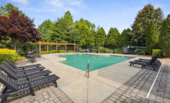 a swimming pool with black chairs and a fence and trees