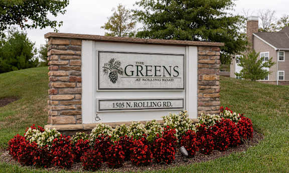 A sign for The Greens at Rolling Road stands in front of a house.