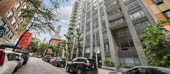 A tall building with a lot of windows is in the middle of a street with cars parked on the side.