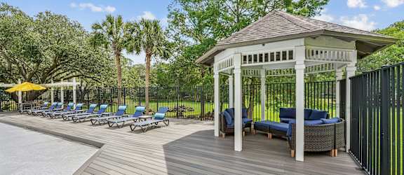 A gazebo with a wooden floor and a white roof is surrounded by a black fence.