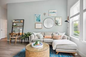 A living room with a grey couch, a wooden table, and a round mirror on the wall.