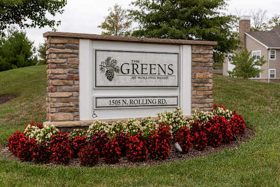 A sign for The Greens at Rolling Road stands in front of a house.