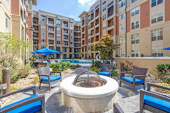 A hot tub sits in the middle of a patio surrounded by chairs and umbrellas.