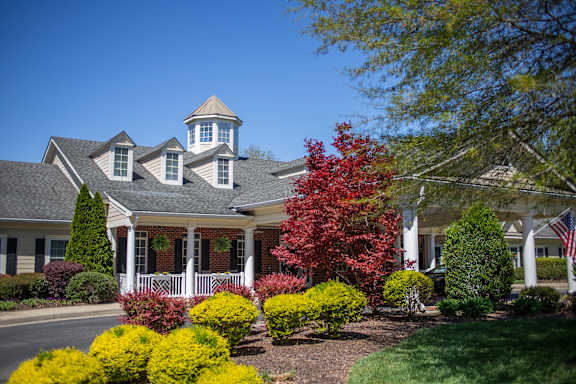 A house with a white fence and a red tree in front.