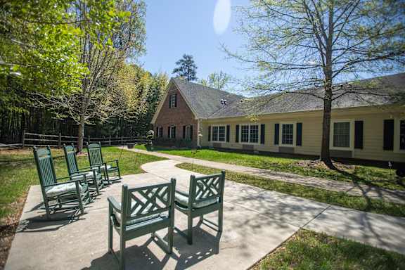A sunny day at a park with a bench and a building in the background.