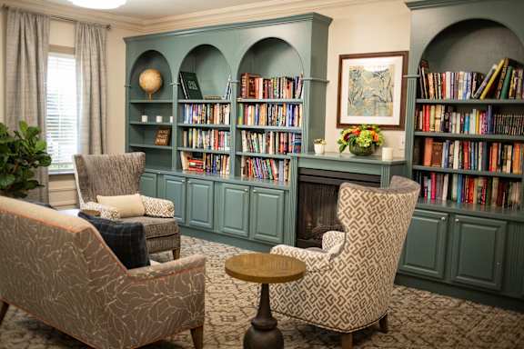 A room with two chairs and a table in front of a bookshelf.
