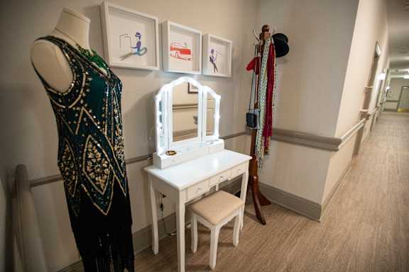 A white vanity table with a mirror and a black dress on a mannequin.