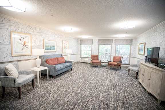 A living room with grey carpet and furniture.at Spring Arbor of Wilson, Wilson, NC