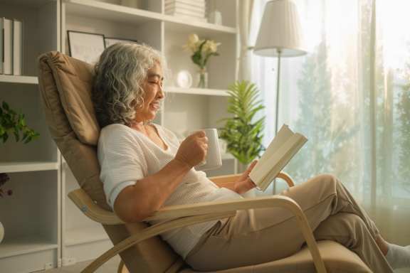 An elderly woman is sitting in a chair and reading a book.