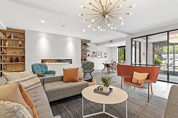 A living room with a grey sofa, a green armchair, a brown armchair, a white coffee table, a fireplace, and a chandelier.