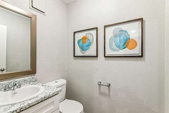 A bathroom with a toilet, sink, and two framed artworks on the wall.