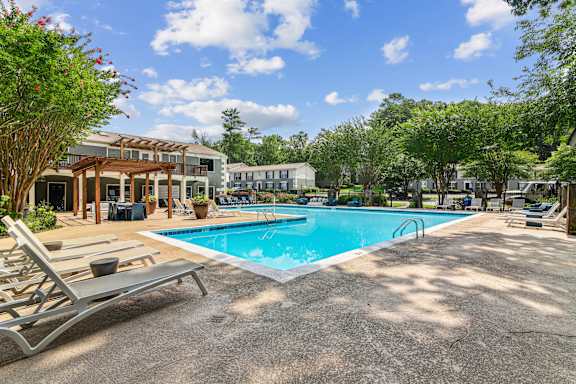 A pool area with sun loungers and a building in the background.