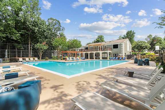 A large swimming pool with sun loungers and a building in the background.