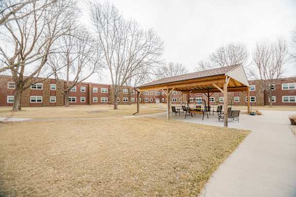 A large grassy area in front of a building with a pavilion and benches.