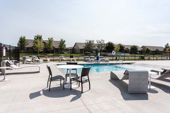 A poolside table and chairs are arranged on a patio.