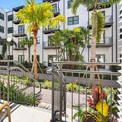 A patio with a table and chairs overlooks a courtyard with plants and trees.