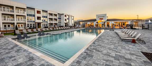 A large outdoor swimming pool surrounded by a stone patio and lounge chairs.