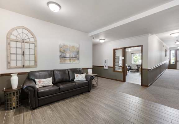 A black leather couch sits in a spacious room with wood flooring and a large window.