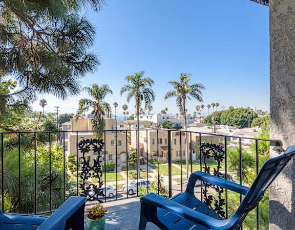 a balcony with two blue lounge chairs and a view of palm trees