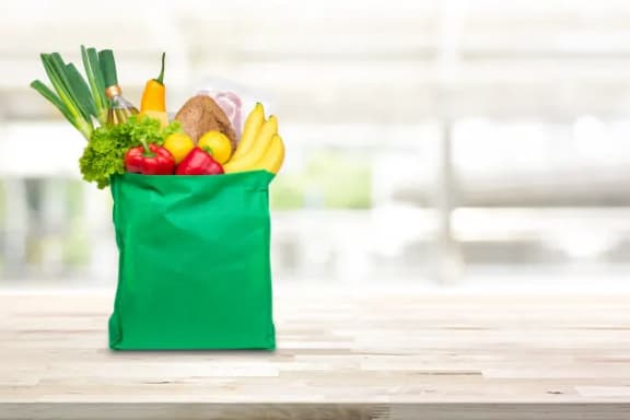 a green bag filled with fruits and vegetables on a table