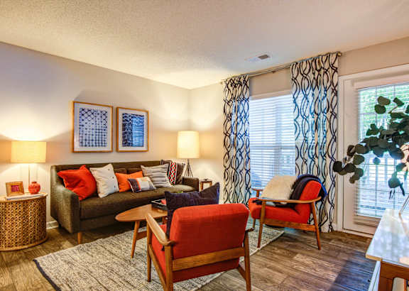 A living room with a red chair and a brown couch at Jamison Park Apartments in North Charleston, SC 29406