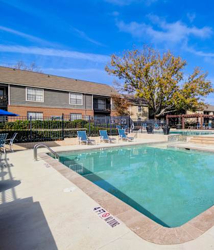 A pool surrounded by chairs and trees.