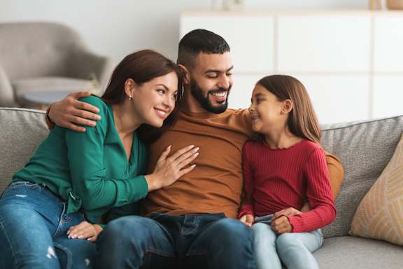 A family of three is sitting closely together on a couch.