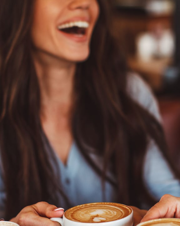 A woman in a beige blazer is holding a white cup.