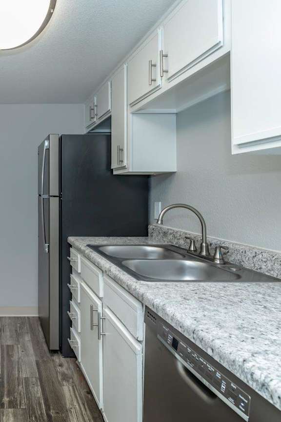 A kitchen with a black fridge and a stainless steel sink.