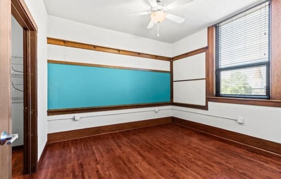 a Horicon School Apartment bedroom with wood flooring, a ceiling fan, wall chalkboard, and large window