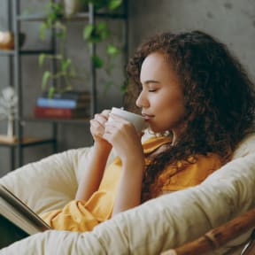 a woman sitting on a couch drinking coffee and reading a book