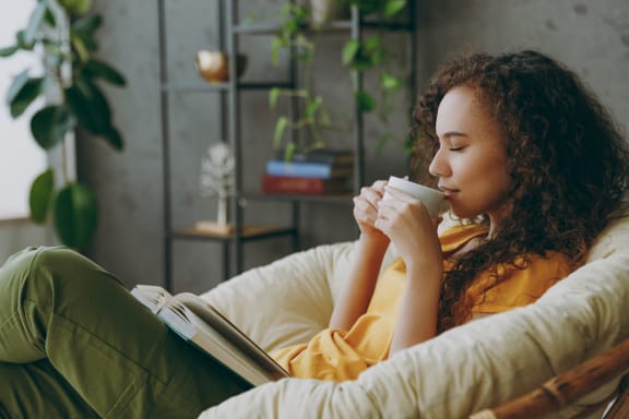 a woman sitting on a couch drinking coffee and reading a book