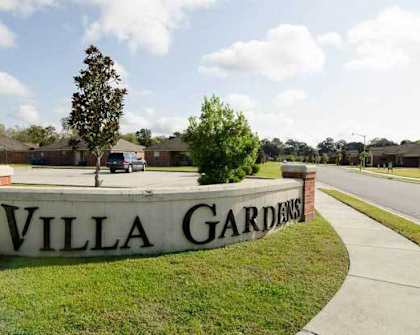 A sign that says "Villa Gardens" in front of a grassy area.