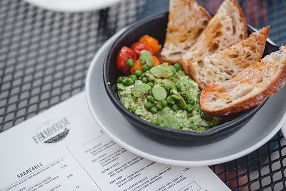 A bowl of guacamole with bread and vegetables on a plate.