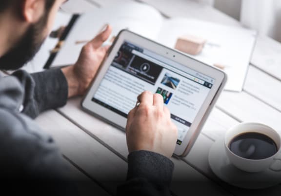 a man sitting at a table with a tablet computer representing in the news