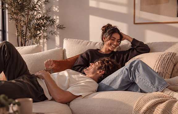 A couple is lying on a couch, with the woman leaning on the man's shoulder.