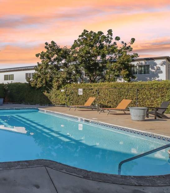 A pool surrounded by a hedge and a mountain in the background.