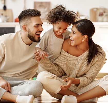 A man and a woman are sitting on the floor with a child, all are smiling and appear to be happy.