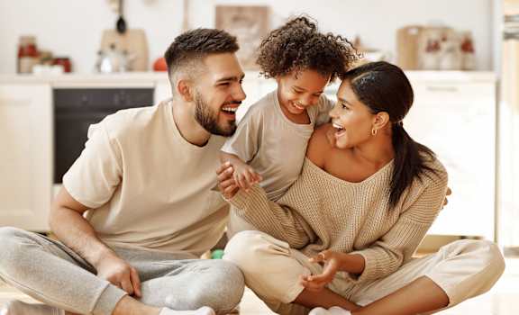 A man and a woman are sitting on the floor with a child, all are smiling and appear to be happy.