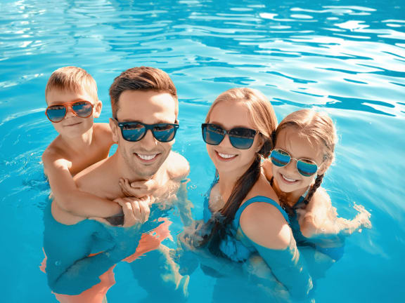 A family of four is enjoying a swim in a pool. at Casa Sole Vita Townhomes, Mesa, AZ