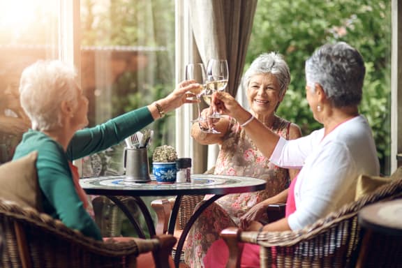 three older women sitting at a patio table drinking wine