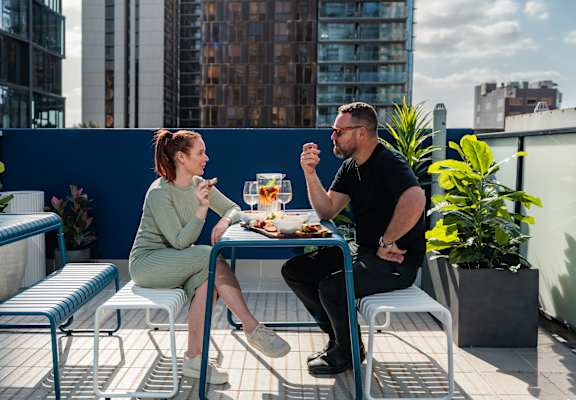 a man and a woman sitting at a table on a balcony eating food