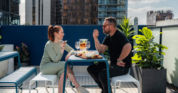 a man and a woman sitting at a table on a balcony eating food